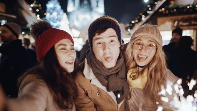 POV Two women and man smiling waving firework take selfie outdoor. Christmas holiday. Multiracial group of friends having fun with sparklers outdoor celebrating merry Christmas xmas and happy new year