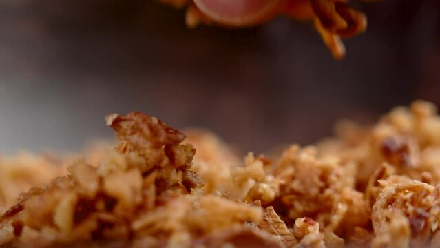Cook hand takes fried onion flakes from a wooden bowl. Dry roasted golden shallot