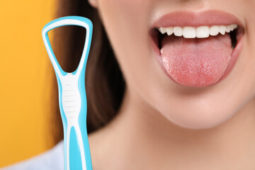 Woman brushing her tongue with cleaner on yellow background, closeup