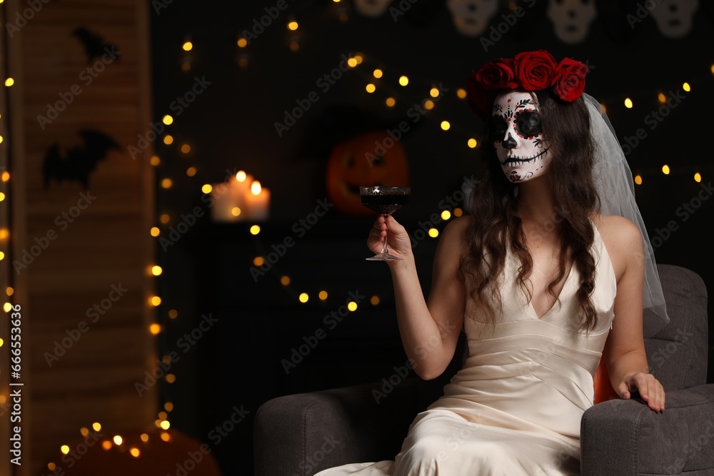 Sticker Young woman in scary bride costume with sugar skull makeup and glass of wine against blurred lights indoors, space for text. Halloween celebration