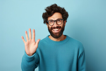 Young handsome man with beard wearing casual sweater and glasses over blue background Waiving saying hello happy and smiling, friendly welcome gesture - obrazy, fototapety, plakaty