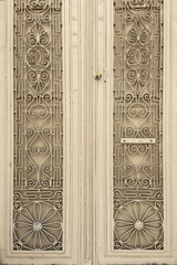 Metal old beige double winged heavy big aged door with wrought iron decorative ornaments, closeup photo of closed doors of an old house