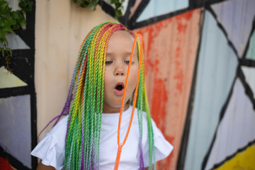 girl with multi-colored afro pigtails inflates soap bubbles against the background of a wall