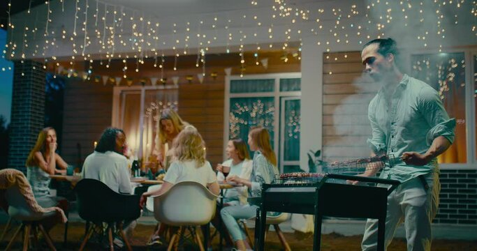 Summer evening with friends in backyard, man grilling meat and multiethnic people dinning 4K, Prores