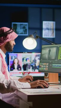 Vertical video Muslim colorist wearing headphones while editing project, creating film montage, working with images and sounds. Man using video cutting technology to process movie on PC workstation