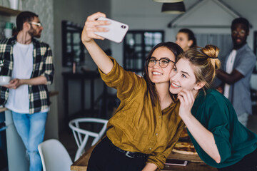 Joyful women taking selfie together with smartphone near multiracial friends