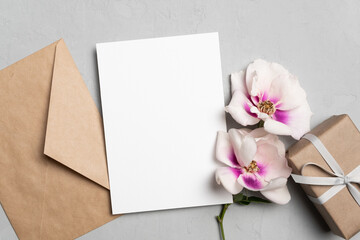 Blank greeting card mockup with gift box, envelope and flowers, card with copy space