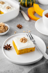Spiced pumpkin cake with walnut and cream cheese frosting sliced into squares on a gray concrete background. Autumn dessert.