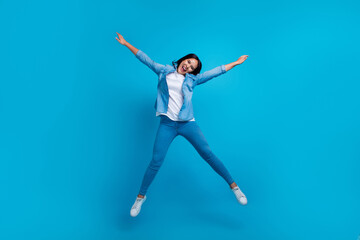 Fototapeta na wymiar Full size photo of overjoyed crazy woman with straight hairdo dressed jeans shirt jumping high hands up isolated on blue background