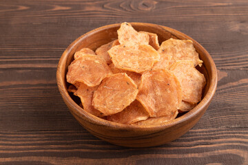 Slices of dehydrated salted meat chips on brown wooden, side view