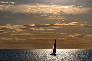 View of a sailing boat at sunset passing in front of the Artruxt Lighthouse, Cuidadela, Menorca, Balearic Islands, Spain