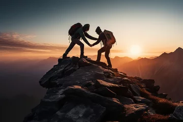 Fototapeten Two mountaineers offer helping hand on a rock ridge at sunrise above a valle © alisaaa