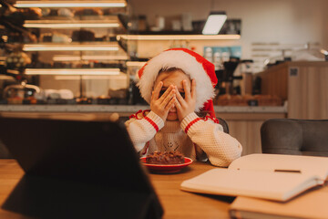 Happy girl enjoys the Christmas holidays, eating a chocolate dessert while looking at a tablet iPad in a cafe.