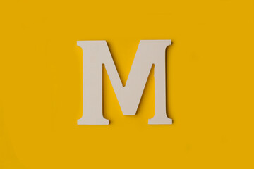 Una letra M hecha en madera blanca sobre un fondo amarillo liso y aislado. Vista superior y de cerca. Copy space - obrazy, fototapety, plakaty