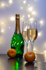 Crystal champagne glasses, tangerines, a bottle of champagne and garland lights in the background. Champagne, tangerines and garlands create a festive mood.