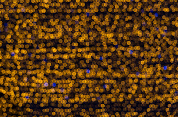 Bokeh made of bright orange lights, interspersed with blue. A large orange garland with rare blue lights in a blur.