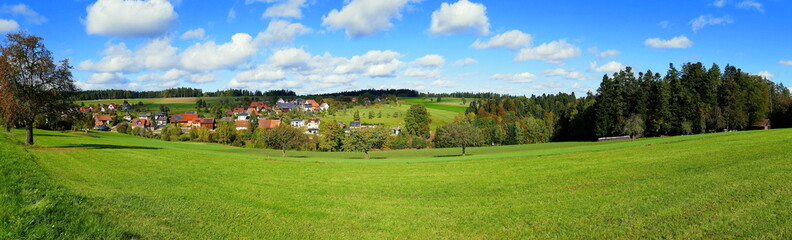 Fototapeta na wymiar Panorama von weiter Landschaft im Schwarzwald im Herbst mit Wiese, Bäumen und Wohnhäusern bei blauem Himmel und weißen Wolken