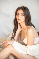 Naklejka premium portrait of beautiful young woman with long hair in white lingerie posing on a beige background