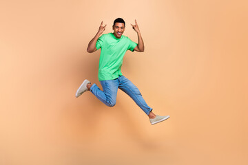 Fototapeta na wymiar Full length photo of satisfied handsome man wear stylish t-shirt jeans jumping show horns symbol isolated on beige color background
