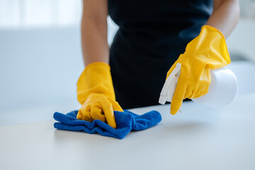 Cleaning desk surface in office with sanitizer spray, wear gloves and wipe the table with a towel, the housekeeper is cleaning the work desk for hygiene because of the Covid-19, cleaning idea.