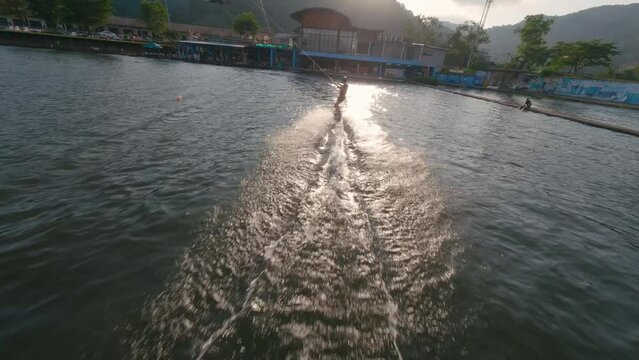 Wakeboarder man ride touch water hand cable wakeboard park lake in mountains. Outdoors sport extreme activity athlete guy doing simple trick springboard backflip training practicing cable wakeboarding