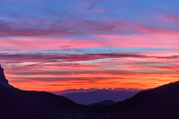 Red sunset over Passo delle Erbe with background of Dolomite peaks. Sky colored with shades of red, orange and blue, aerial view from high altitude.