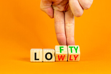 Lofty or lowly symbol. Concept words Lofty Lowly on wooden block. Beautiful orange table orange background. Businessman hand. Business lofty or lowly concept. Copy space.