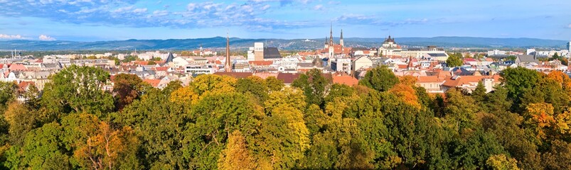Obraz premium Panoramic view through autumn-coloured trees to the towers and temples of the centre of Olomouc, the historical centre of Moravia, Czech republic, UNESCO site. Autumn, sunny day, view from the air.