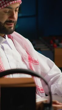 Vertical video Smilling arab man doing online shopping, using computer to look up tech products to buy. Middle Eastern person adding credit card payment method on secure website, ordering with instant