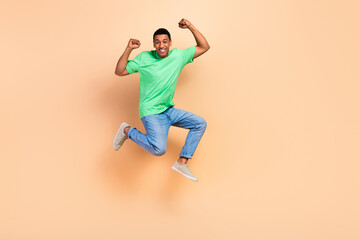 Fototapeta na wymiar Full length photo of ecstatic overjoyed man wear stylish t-shirt jeans jumping raising fists win bet isolated on beige color background