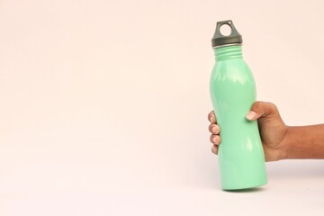 Close-up of male hand holding green reusable stainless thermo water bottle isolated on background...