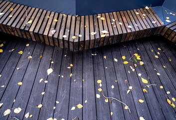A wooden bench with a platform in a park with yellow leaves.