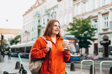 Young beautiful woman with coffee walking in street. Take away or delivery concept. Copy space. Autumn lifestyle.
