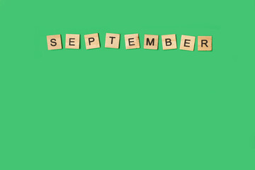 Bloques de madera formando la palabra septiembre sobre un fondo verde liso y aislado. Vista superior. Copy space