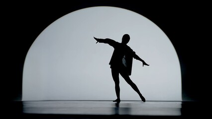 Contrasting silhouette of a young woman performing contemporary dance in the studio. Female figure...