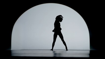Contrasting silhouette of a young woman performing contemporary dance in the studio. Female figure dancing under a spotlight. Full size.