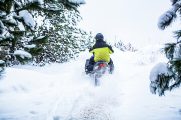 Fototapeta na wymiar Snowmobile in snow. Concept winter sports. Man is riding snowmobile in mountains. Pilot on a sports snowmobile in a mountain forest. Athlete rides a snowmobile in the mountains