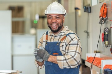 Portrait of Young black skin carpenter finished creating smiles to camera. Happy Carpenter holds wooden planks for build furniture in carpentry workshop. foreman carpenter standing in shop.