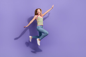 Full size photo of pretty teenager blonde girl jump hands fly wings plane wear trendy striped outfit isolated on purple color background