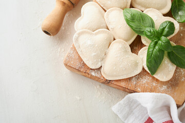 Italian ravioli pasta in heart shape. Tasty raw ravioli with flour and basil on white background. Food cooking ingredients background. Valentines or Mothers Day lunch ideas. Top view with copy space.