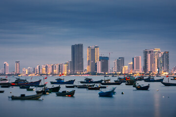 Da Nang cityscape at twilight. Fishing boat moored in port against illuminated coast with modern buildings.. - obrazy, fototapety, plakaty