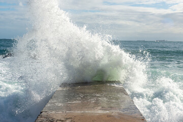 Sea waves hit the cement pier on a beach. Wild nature.