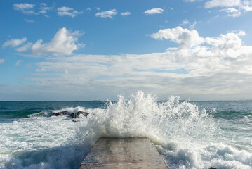 Waves from the rough sea crash heavily onto a beach pier. Wild nature.