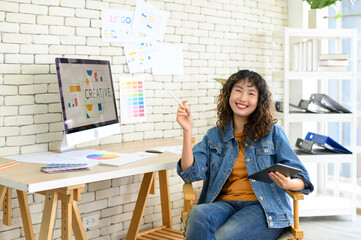 Asian female artist drawing something on graphic tablet. graphic designer working at office. Looking at camera.