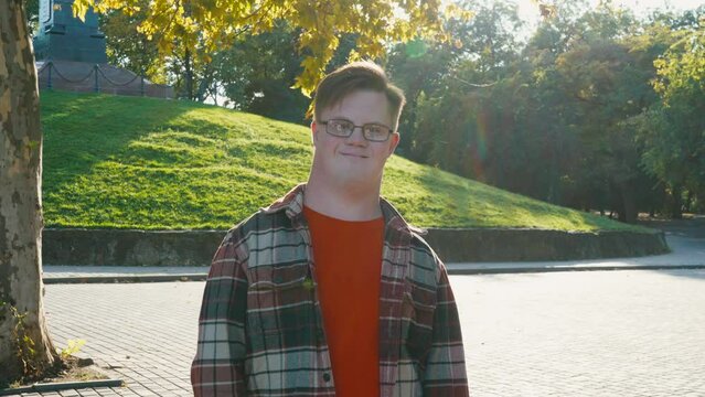 Portrait of young man with down syndrome in checkered shirt walking outdoors in the public park. Man with trisomy 21 illness. Disabled guy having a walk