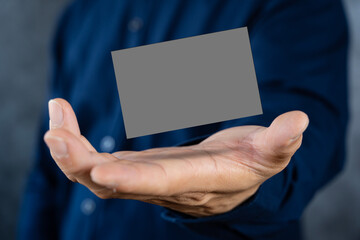 Man holding a dark gray business card against a concrete wall Mature male hand holding a blank business card in front of the camera.