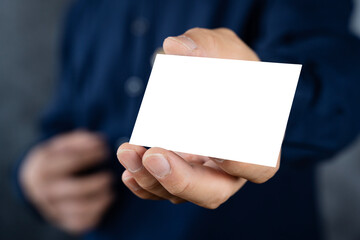 Man holding white business card on concrete wall background, adult man hand holding empty business card in front of camera.