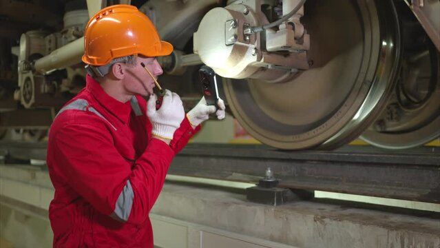 Electric train engineer use a walkie-talkie to inspect electric train machinery according to inspection round after the electric train is parked in the electric train's repair shop