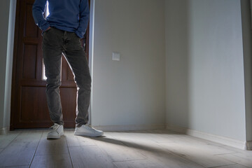 a guy is standing by the door in jeans,a guy in gray jeans and white sneakers is standing at the door