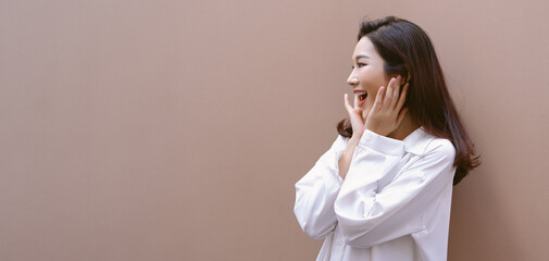 Side view of beautiful excited Asian woman shout out loud wow with hands on isolated beige background. Asia girl holding touching her cheeks with two hands copy space. Photo banner for website, Mockup - obrazy, fototapety, plakaty